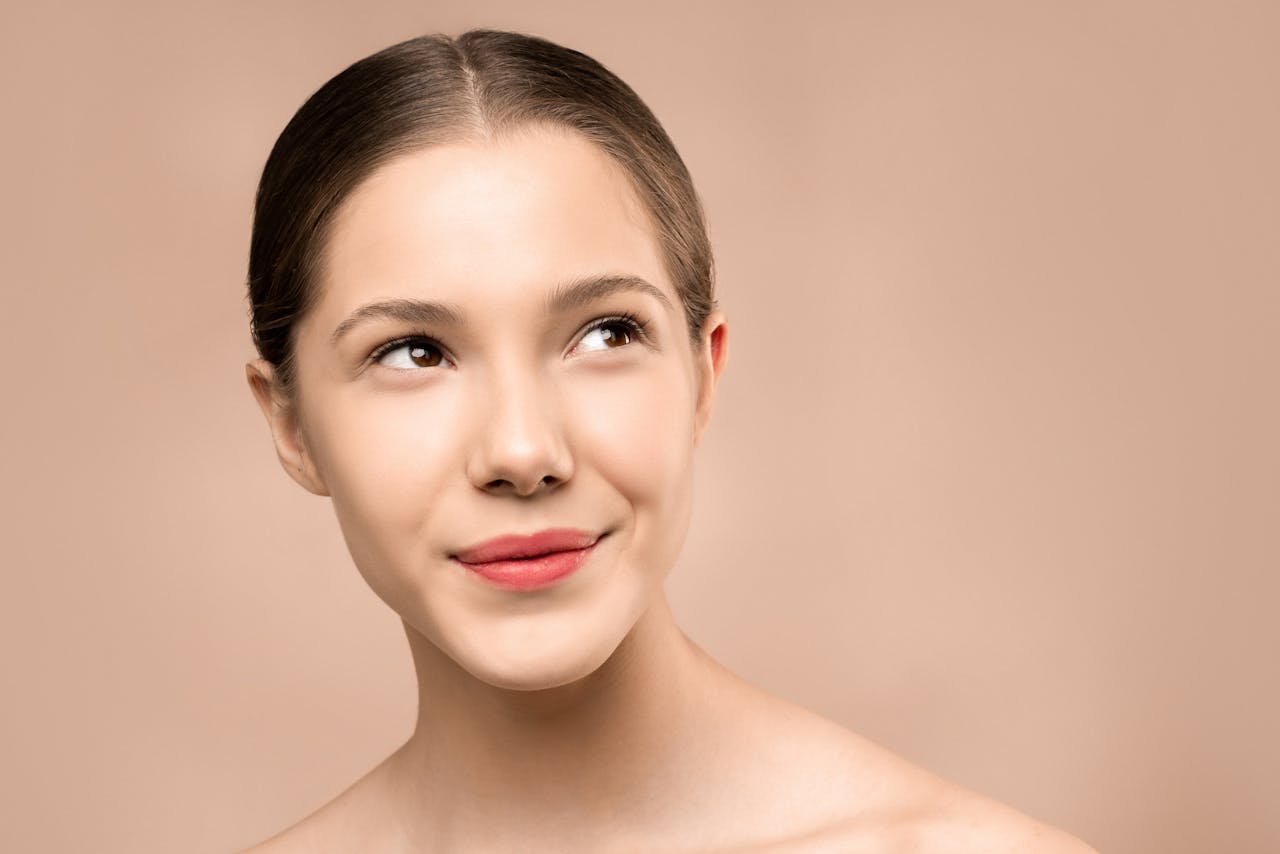 heros-img Portrait of a young woman smiling with radiant, flawless skin against a nude background.